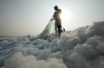 Un pescador tira de su red en la orilla de la playa Marina, llena de espuma, en Chennai (India), el 23 de noviembre de 2018.