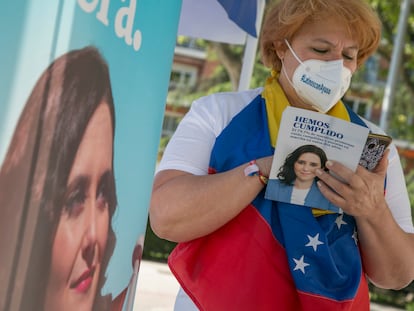 Una mujer arropada con una bandera de Venezuela lee un folleto de Isabel Díaz Ayuso el domingo en el distrito de Chamartín.