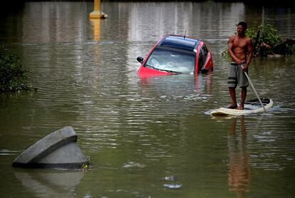 Un hombre se desplaza este jueves en una tabla de paddle surf por una zona inundada tras un fuerte temporal en el barrio de Barra da Tijuca, en Río de Janeiro (Brasil). Al menos cinco personas han perdido la vida y hay varios desaparecidos. La ciudad ha sido declarada en "estado de crisis".