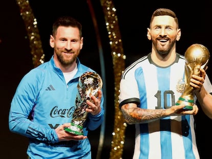 Messi, with the World Cup trophy, next to a statue of the player.