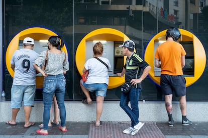 Varios clientes realizan operaciones en un cajero automático de CaixaBank en Madrid, en una fotografía de archivo.