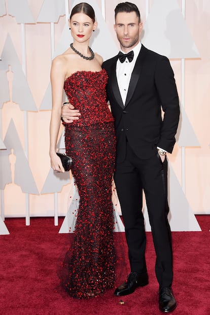 Adam Levine, nominado por la canción Lost Stars de Begin Again, optó por esmoquin de Giorgio Armani. Behati Prinsloo, con moño pulido y vestido de Armani Privé.