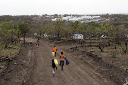 Niños de Sudán del Sur transportan jarras de agua por un camino del campo de refugiados de Impevi. Al fondo están las carpas comunales para el centro de procesamiento.