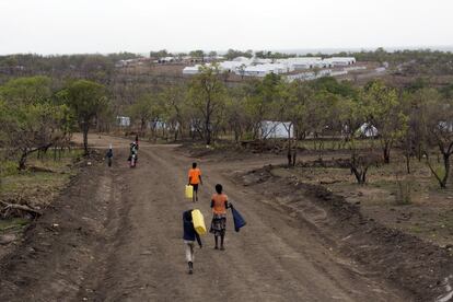 Niños de Sudán del Sur transportan jarras de agua por un camino del campo de refugiados de Impevi. Al fondo están las carpas comunales para el centro de procesamiento.