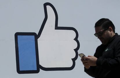 Un hombre usa su móvil ante el logo de "Me gusta" popularizado por Facebook.