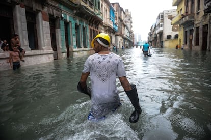 Un joven cubano lleva unas botas de agua en los brazos mientras camina por una calle de La Habana inundada tras el paso del huracán Irma.