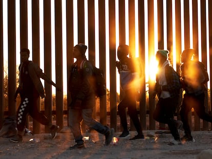 Migrantes caminan frente al muro fronterizo de Estados Unidos en Lukeville, Arizona, en diciembre de 2023.