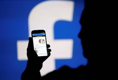 FILE PHOTO: A man is silhouetted against a video screen with an Facebook logo as he poses with an Samsung S4 smartphone in this photo illustration August 14, 2013. REUTERS/Dado Ruvic/File Photo