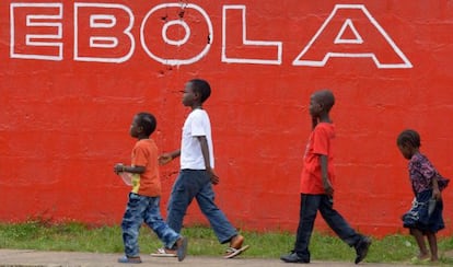 Unos ni&ntilde;os pasan frente a un cartel que advierte contra el &eacute;bola en Monrovia (Liberia).