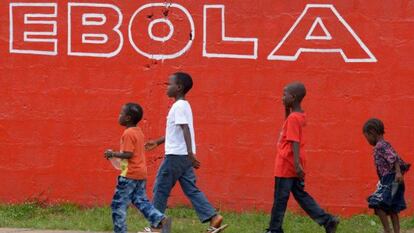 Unos ni&ntilde;os pasan frente a un cartel que advierte contra el &eacute;bola en Monrovia (Liberia).