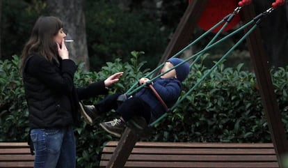 Una mujer fuma un cigarrillo ante un columpio ocupado por un niño en el parque del Retiro de Madrid