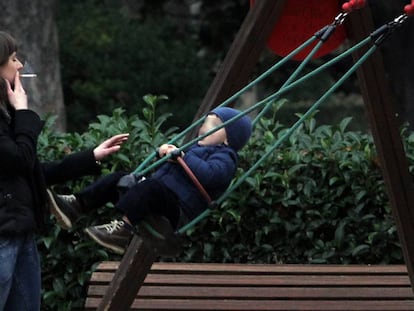 Una dona fuma un cigarret davant d'un nen en un parc.