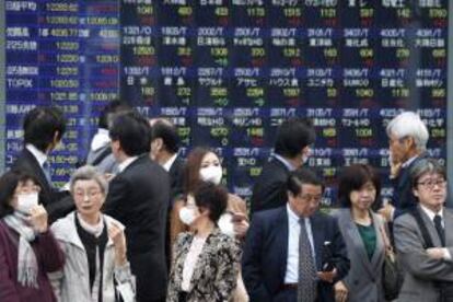 Viandantes caminan frente a una pantalla que muestra los valores de las acciones al cierre de la Bolsa de Tokio. EFE/Archivo