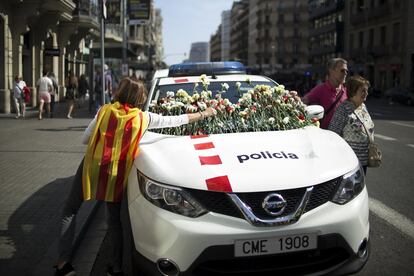 Una mujer deposita claveles en el parabrisas de un coche de los Mossos d'Esquadra en Barcelona.