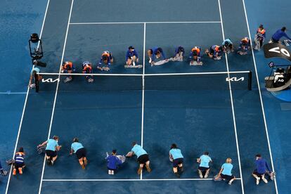 Recogepelotas secan la pista después de que la lluvia interrumpiera el partido de cuartos de final masculino entre el italiano Jannik Sinner y el griego Stefanos Tsitsipas en el torneo de tenis del Open de Australia en Melbourne.