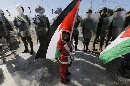 Un niño palestino vestido como Papá Noel sostiene una bandera palestina delante de un grupo de soldados israelíes durante una protesta en contra de la polémica barrera israelí en la aldea cisjordana de Al-Masara, cerca de Belén.