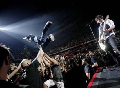 Un seguidor de Green Day se lanza desde el escenario al público mientras Billie Joe Armstrong toca la guitarra.