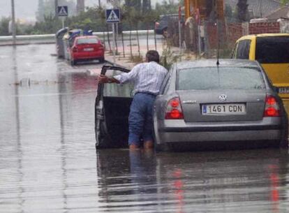 Un hombre junto a su vehículo en una calle inundada de la capital murciana debido a las fuertes lluvias caídas en la región de Murcia.