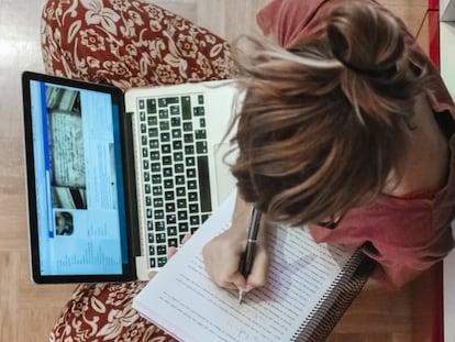 Una joven escribe a mano mientras consulta su ordenador.