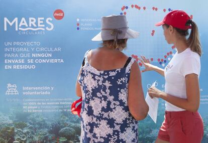 Una voluntaria explica el proyecto Mares Circulares a una ciudadana en una playa de Torremolinos (Málaga).