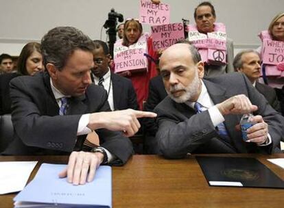 Geithner (izquierda), junto a Bernanke ayer en la comparecencia. Detrás, un grupo protesta por la crisis.