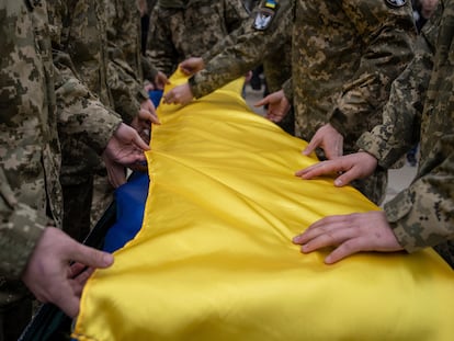 Ukrainian servicemen fold the national flag over the coffin of their comrade Andrii Neshodovskiy during the funeral ceremony in Kyiv, Ukraine, Saturday, March 25, 2023.