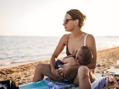 Una mujer da el pecho en la playa.