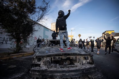 Manifestantes sobre un coche de policía quemado, el sábado en Los Ángeles.