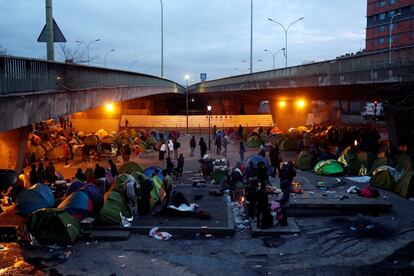 Un grupo de inmigrantes espera a ser evacuado por la policía francesa de un campamento improvisado establecido bajo el puente de la 'Porte de la Chapelle', en París. Los inmigrantes serán trasladados a gimnasios de la región para examinar su situación sanitaria y administrativa.