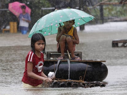 Unas niñas en una balsa improvisada tratan de cruzar una carretera de Butan en la isla filipina de Mindanao, asolada por las inundaciones.