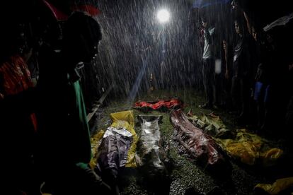 Un grupo de personas se reúnen bajo la lluvia alrededor de los cuerpos sin vida de unos refugiados rohinyás tras morir ahogados en la playa de Inani, cerca de Cox's Bazar (Bangladés), el 28 de septiembre de 2017.