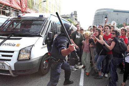 Un <i>mosso</i> levanta su porra contra varios manifestantes en la plaza de Catalunya.
