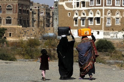Mujeres yemeníes cargan con garrafas de agua mientras una niña esparce agua de una botella. Los cortes en el suministro de agua en Saná (Yemen) son habituales.