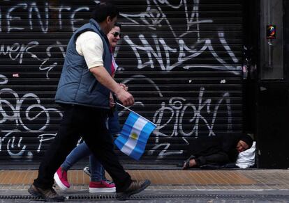 Mulher dorme na calçada enquanto pessoas caminham durante a celebração do bicentenário da independência argentina, em Buenos Aires.