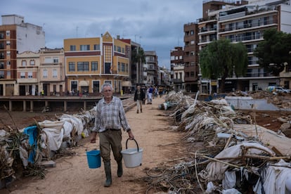 Un hombre transporta agua mientras cruza cruza la Rambla del Poyo, el barranco que canaliz la riada que se produjo el pasado martes, a travs uno de los puentes que conectan los dos sectores deL pueblo de Paiporta, el jueves 31 de octubre de 2024.