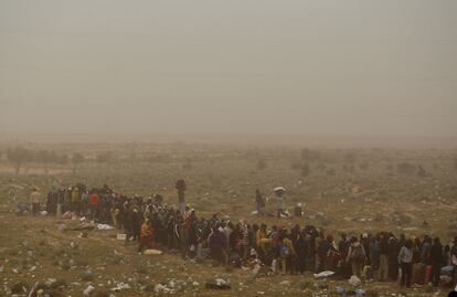 Un grupo de refugiados hace cola para obtener sustento en medio de una tormenta de arena en Ras Jdir.