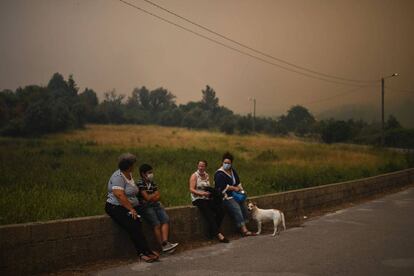 Residents, alguns amb màscara a la cara, esperen asseguts mentre l'incendi segueix amenaçant el poble de Torgal.