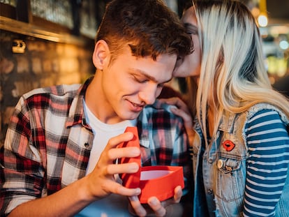 Un chico abriendo un pequeño corazón, mientras la chica le dice algo al oído.