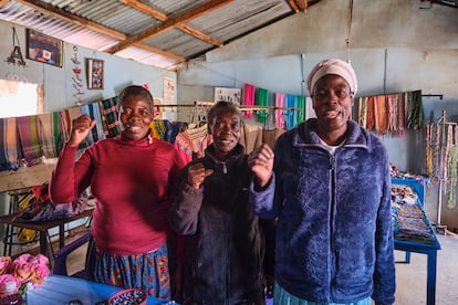 Rosemary (izquierda) y otras dos compañeras del Karibuni Power Women Group posan con el puño izquierdo en alto, en una edificación del barrio marginal de Kibera (Nairobi), donde venden bisutería y productos fabricados con tejidos africanos.