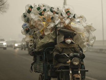 Un motorista conduce su motocarro por Shangháilleva repleto de botellas de plástico para ser recicladas.