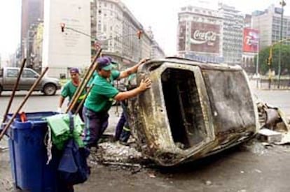 Trabajadores de limpieza retiran un coche incendiado en el centro de Buenos Aires durante los disturbios.