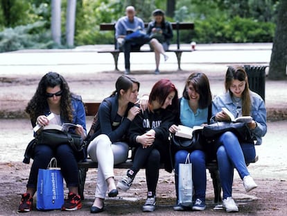 Grupo de jovens l&ecirc; num banco na Feira do Livro de Madri. 