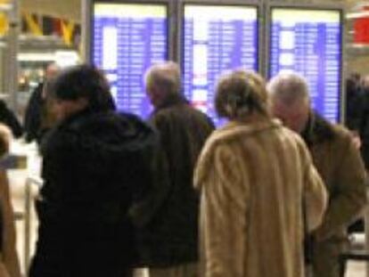 Varios viajeros miran los paneles de información de sus vuelos en la terminal 4 del aeropuerto de Barajas (Madrid)