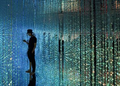 Un visitante utiliza su teléfono inteligente mientras contempla la instalación digital 'Wander through the Crystal Universe' ('Vagar por el universo de cristal) presentado por el colectivo artístico teamLab en el evento 'A World of Wonders' en Tokio (Japón).
