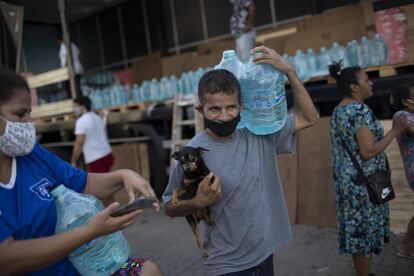 Edilson da Silva lleva agua embotellada donada por Cruz Roja, en la favela de Rocinha, en Río de Janeiro (Brasil). Las autoridades sanitarias han confirmado este jueves casi 60.000 casos nuevos de coronavirus y más de 1300 muertes.