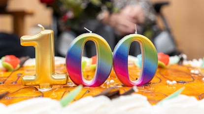 A close-up of a birthday cake adorned with vibrant icing flowers and glistening number '100' candles, symbolizing a grand celebration of 100 years.