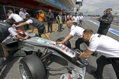 Varios mecánicos de Mercedes empujan el coche de Michael Schumacher, ante la mirada del dueño del equipo, Ross Brawn.