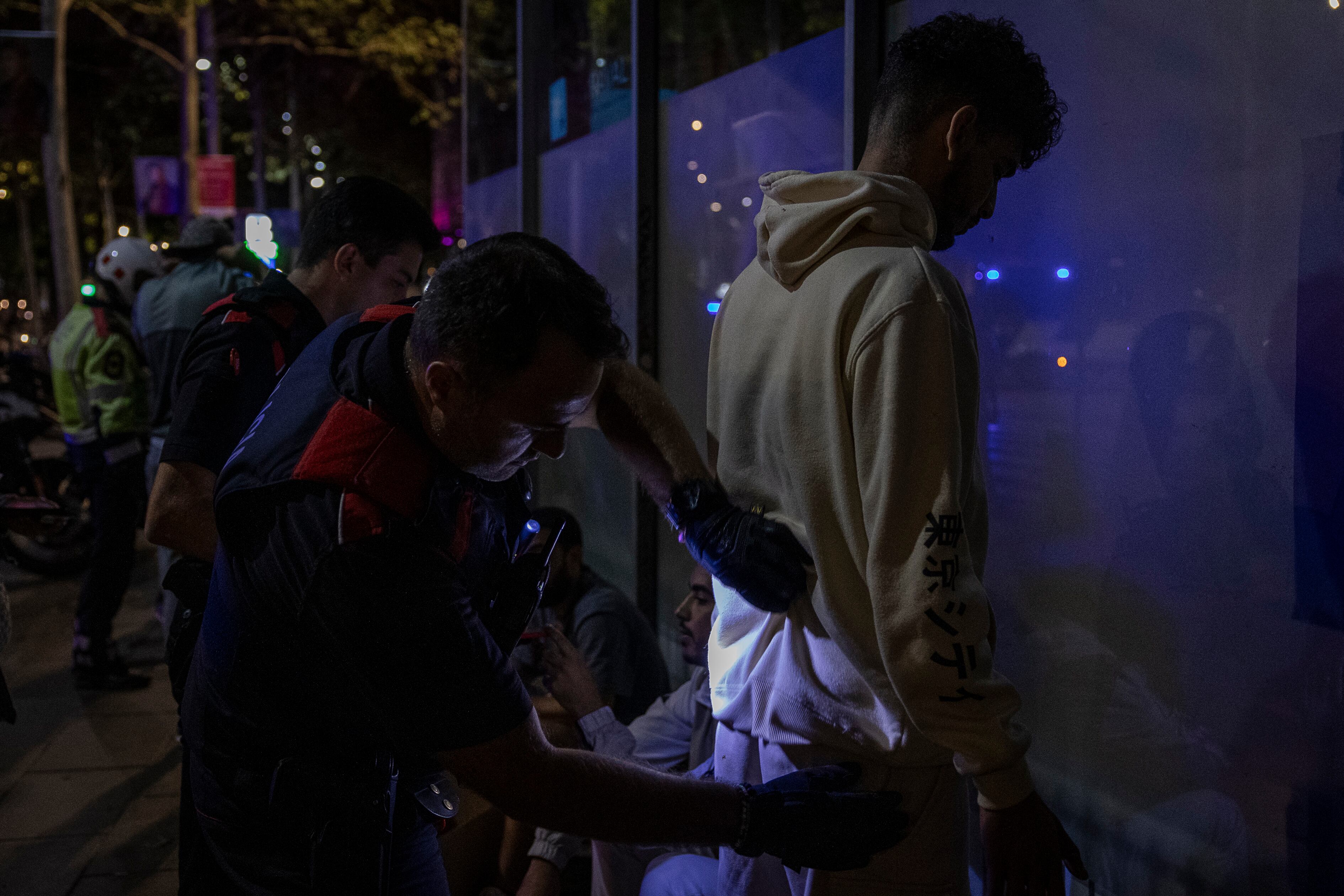 Un agente de los Mossos d'Esquadra registra a un joven en la Rambla del Raval, este viernes.