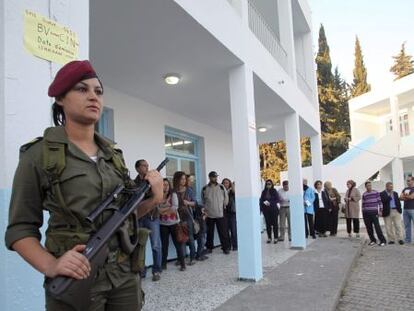 Una mujer soldado resguarda el exterior de un colegio electoral donde varias personas esperan su turno para entrar a votar el domingo.