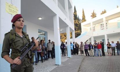 Una mujer soldado resguarda el exterior de un colegio electoral donde varias personas esperan su turno para entrar a votar el domingo.